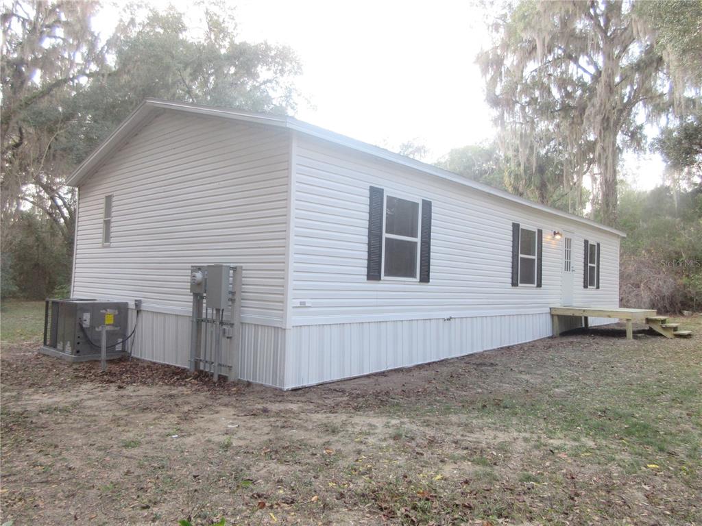 A white manufactured home with black shutters sits on a dirt lot with trees — 2960 NE 159TH PLACE, CITRA, FL