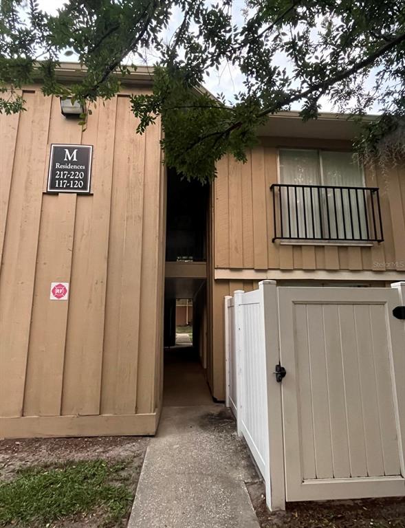 The exterior of a tan apartment building features a walkway between units and a white fence — 507 NW 39TH ROAD UNIT 220, GAINESVILLE, FL