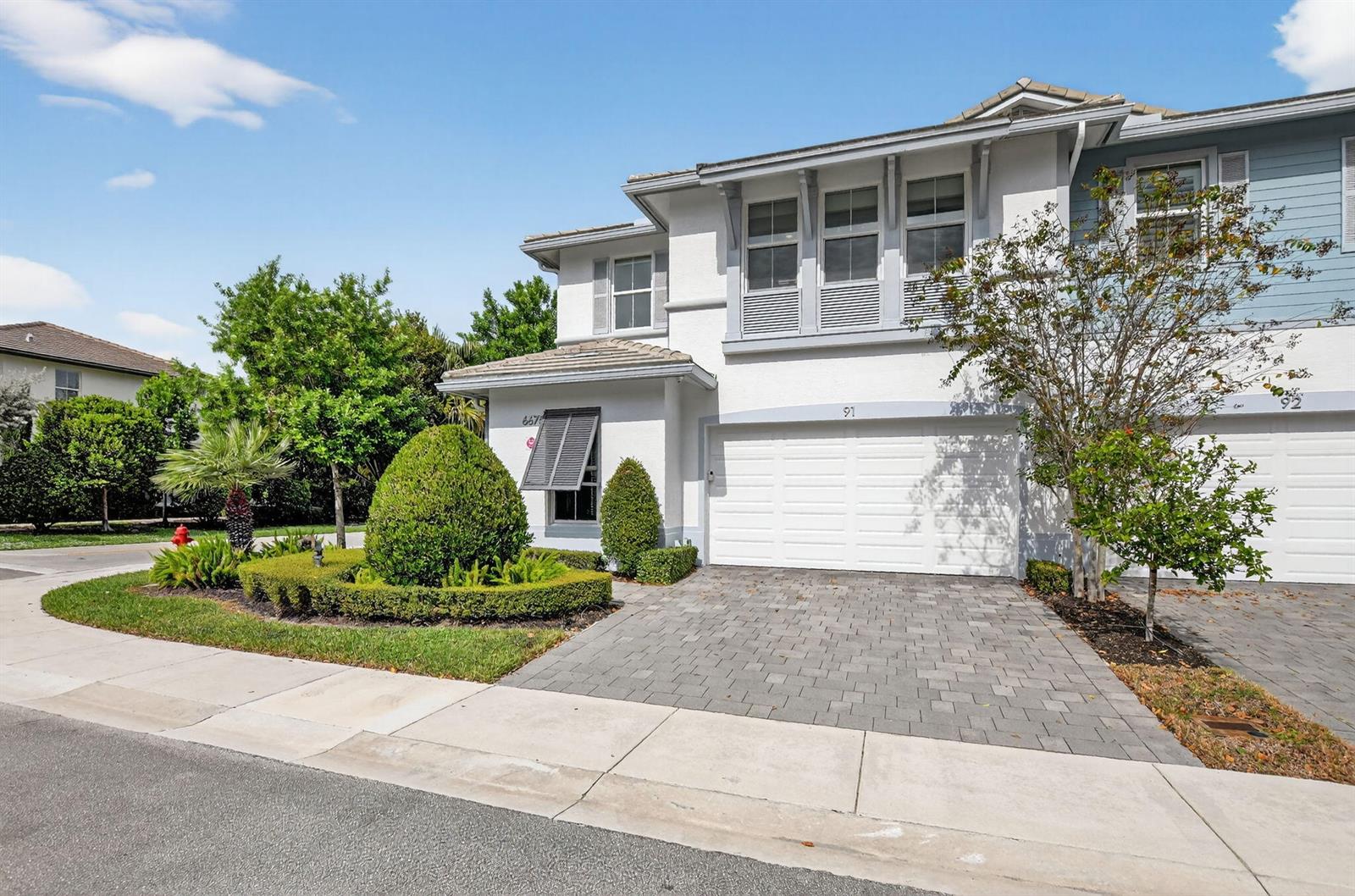 A two-story white stucco townhouse features a paved driveway, a garage, and landscaped front yard — 6675 Quiet Wave Trail # 91, Boca Raton FL 33433, BOCA RATON, FL