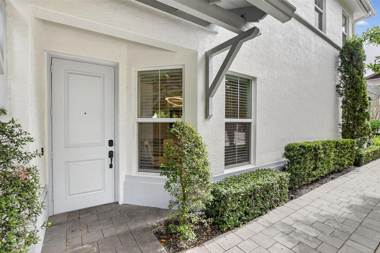 A white exterior wall features a front door, two windows, and a paved walkway — 6675 Quiet Wave Trail # 91, Boca Raton FL 33433, BOCA RATON, FL