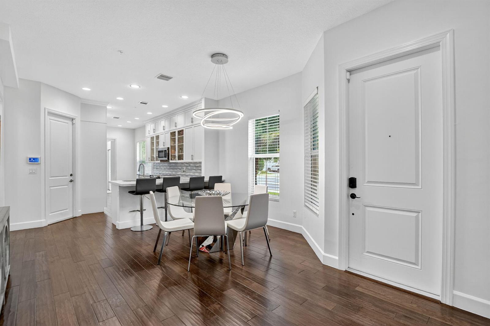 A modern dining area with a glass table, white chairs, and an adjacent kitchen island — 6675 Quiet Wave Trail # 91, Boca Raton FL 33433, BOCA RATON, FL