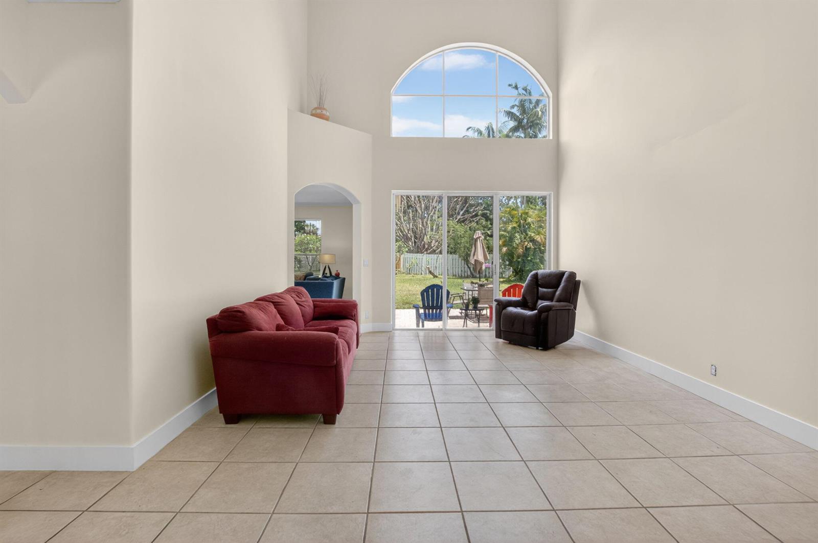 A living room with high ceilings, tile flooring, a red sofa, and a large arched window — 6207 Shadow Tree Lane, Lake Worth FL 33463, LAKE WORTH, FL