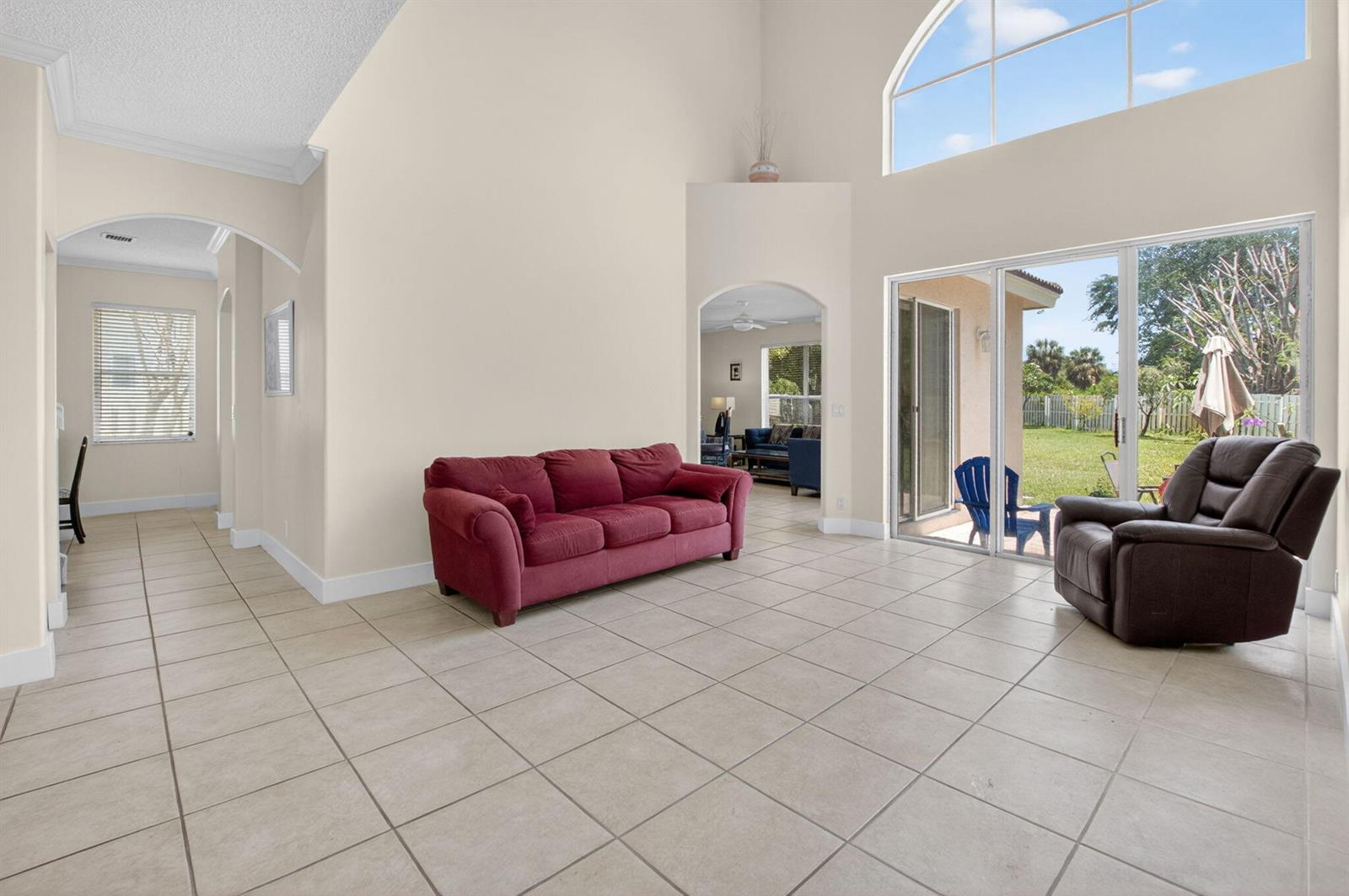A living room with tile floors, a red sofa, a recliner, and large sliding glass doors — 6207 Shadow Tree Lane, Lake Worth FL 33463, LAKE WORTH, FL