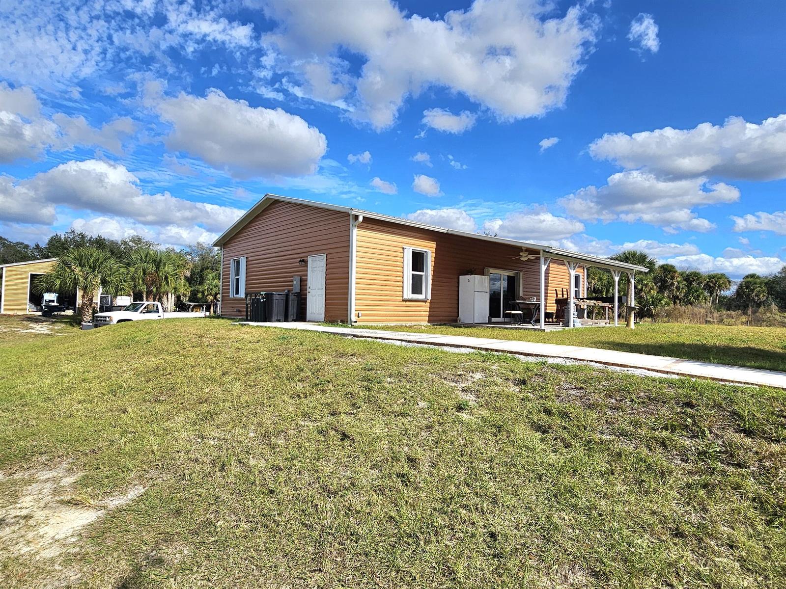 A tan-sided house with a covered porch and a concrete walkway sits on a lawn — 19835 NW 266 Street, Okeechobee FL 34972, OKEECHOBEE, FL