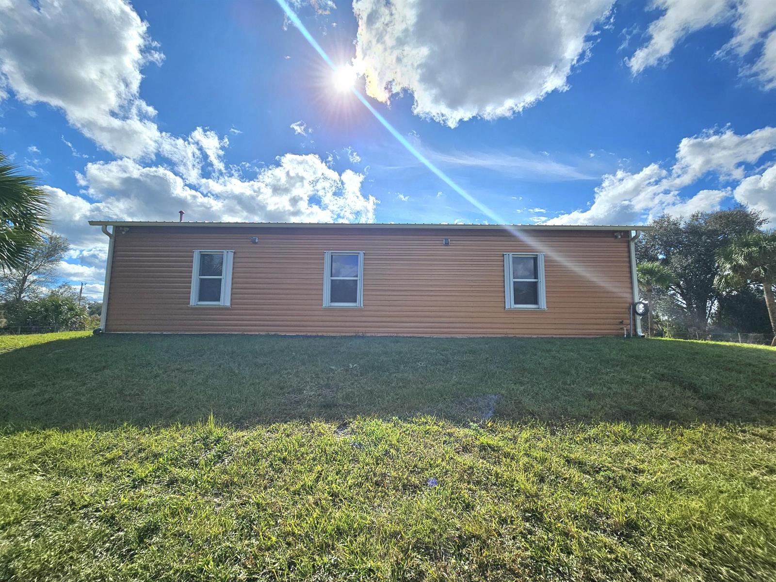 A side view of a tan, single-story house with three windows and a metal roof — 19835 NW 266 Street, Okeechobee FL 34972, OKEECHOBEE, FL