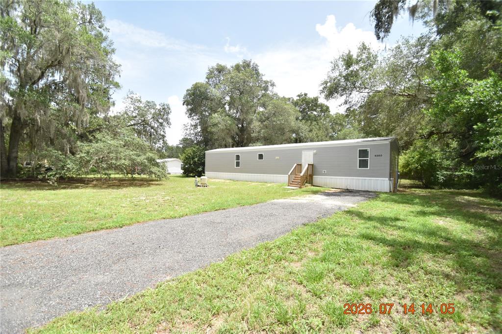 A single-story manufactured home with gray siding sits on a gravel driveway near trees — 6560 W AVOCADO STREET, CRYSTAL RIVER, FL