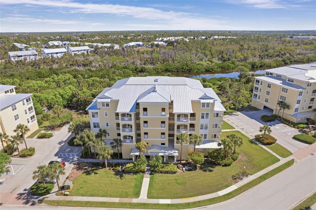 An aerial view shows a multi-story yellow apartment building with a metal roof and landscaping — 8561 AMBERJACK CIRCLE UNIT 302, ENGLEWOOD, FL
