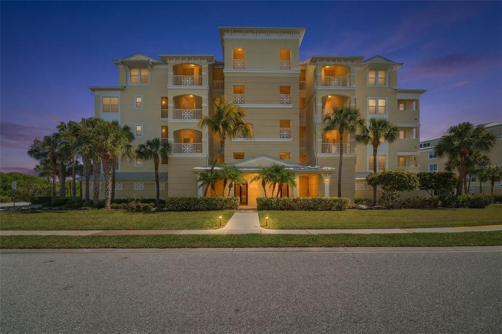 A multi-story beige apartment building with balconies and palm trees at dusk — 8561 AMBERJACK CIRCLE UNIT 302, ENGLEWOOD, FL