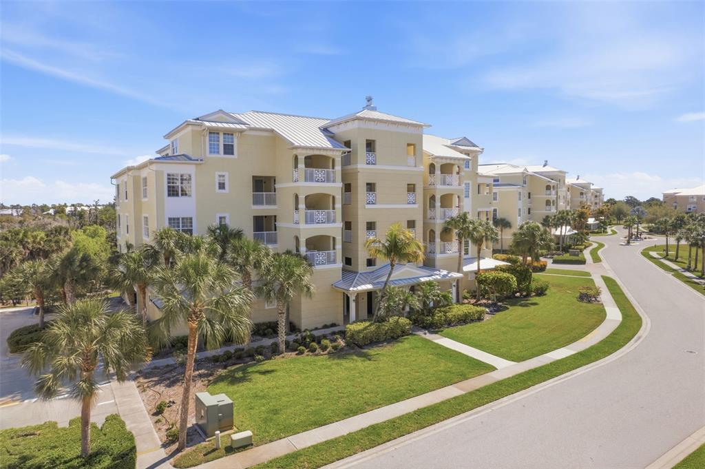 An aerial view shows a multi-story yellow apartment building surrounded by palm trees and landscaping — 8561 AMBERJACK CIRCLE UNIT 302, ENGLEWOOD, FL