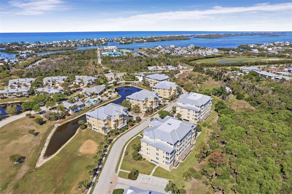 An aerial view shows multi-story apartment buildings surrounded by ponds, green space, and coastal water — 8561 AMBERJACK CIRCLE UNIT 302, ENGLEWOOD, FL