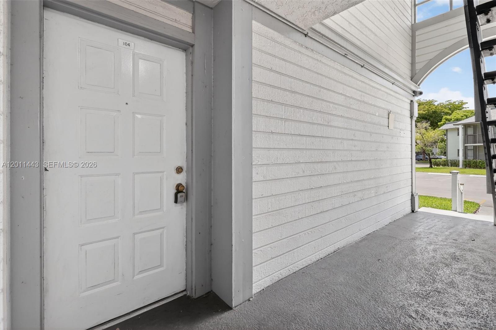 A white door labeled 104 is set in a white horizontal-sided wall on a walkway — 20731 NE 4th Pl # 104, Miami FL 33179, MIAMI, FL