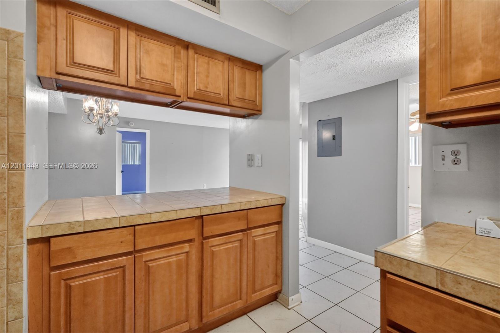 A kitchen features wood cabinets, tiled countertops, and a pass-through window to another room — 20731 NE 4th Pl # 104, Miami FL 33179, MIAMI, FL