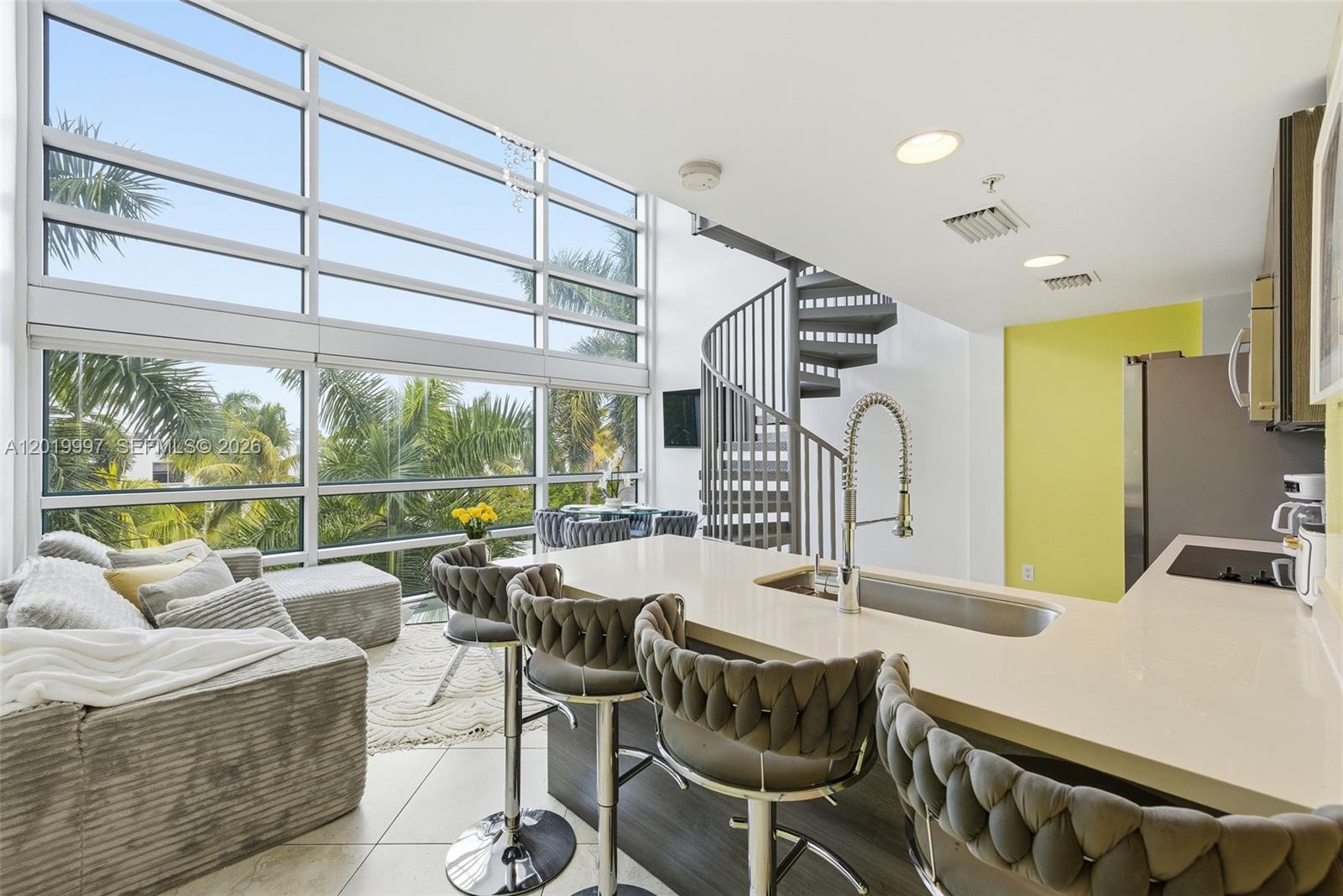 A modern kitchen with a breakfast bar and spiral staircase overlooks a living area — 421 Meridian Ave # 16, Miami Beach FL 33139, MIAMI BEACH, FL