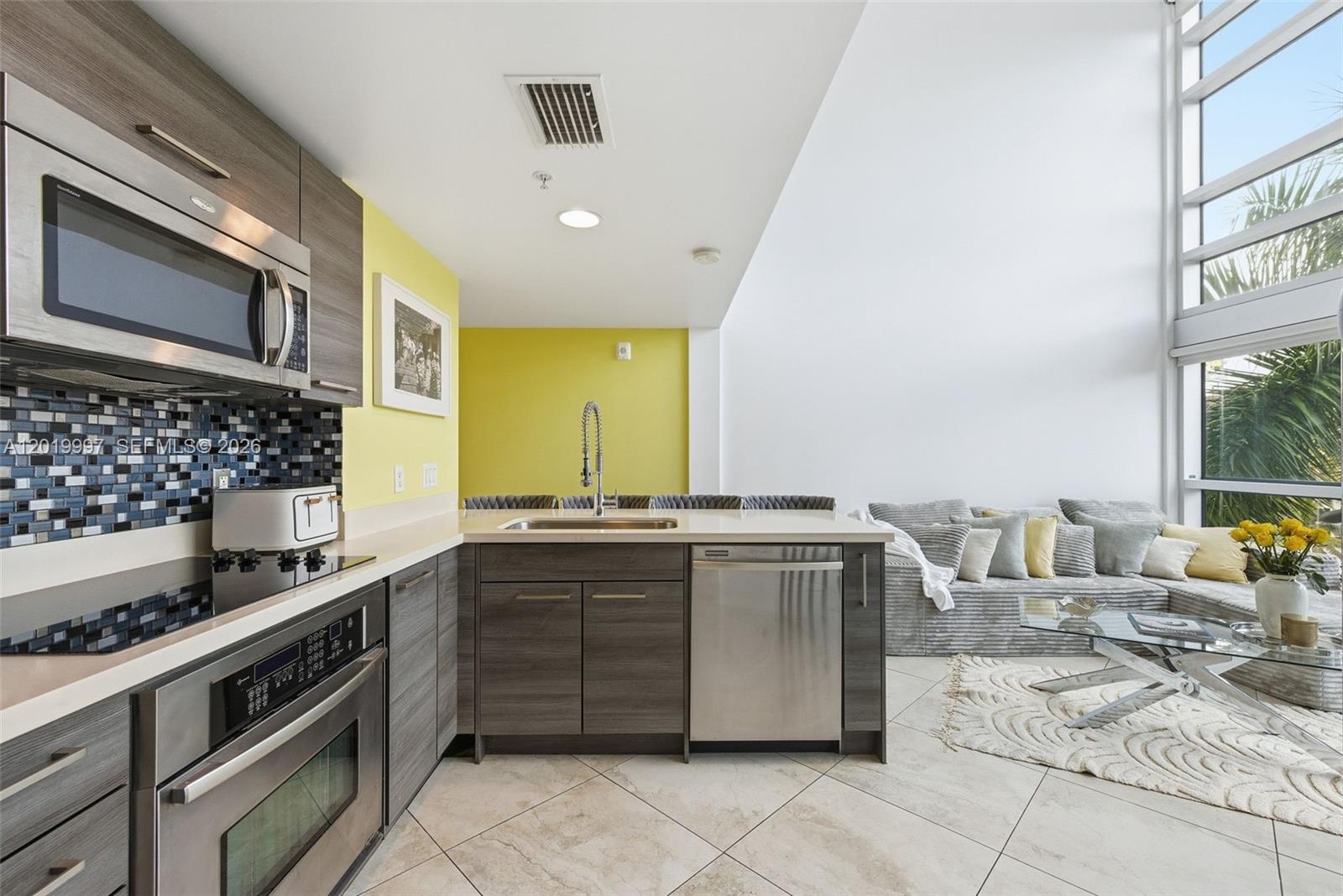 A modern kitchen with dark wood cabinets and a yellow wall opens into a living area — 421 Meridian Ave # 16, Miami Beach FL 33139, MIAMI BEACH, FL