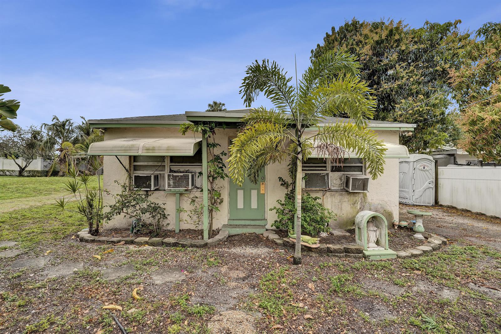 A small, single-story stucco house with a green door, metal awnings, and a palm tree — 1412 B Nw 7 Street, Pompano Beach FL 33069, POMPANO BEACH, FL