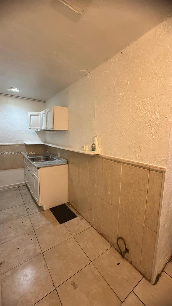 This kitchen features white cabinets, a small sink, and beige tiled walls and floors — 725 Opa Locka Blvd # C, Opa-Locka FL 33054, OPA-LOCKA, FL