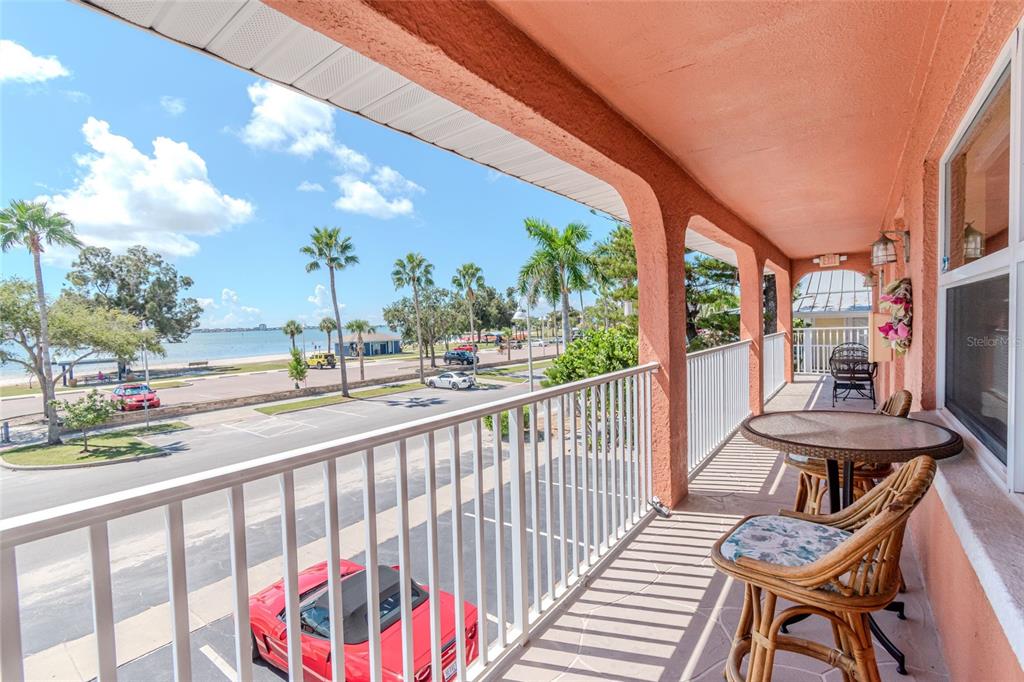 A covered balcony with wicker furniture overlooks a parking lot, palm trees, and the ocean — 5605 SHORE BOULEVARD S UNIT 1B, GULFPORT, FL