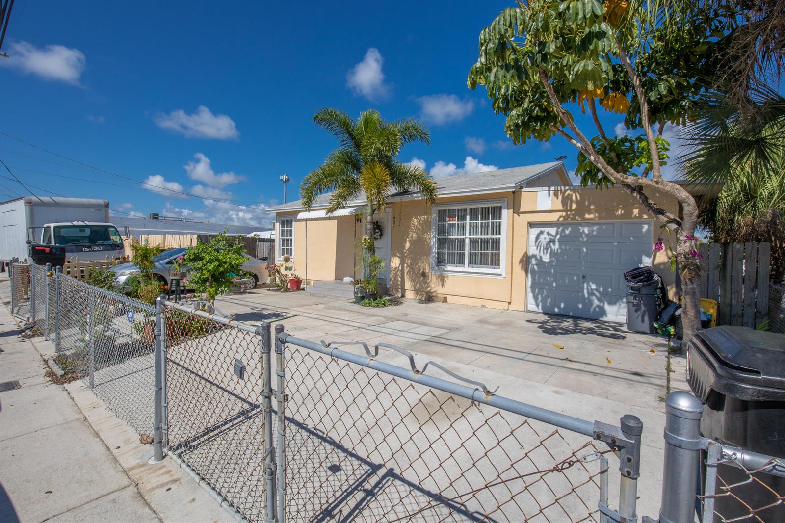 A single-story yellow house features a palm tree, a concrete driveway, and a chain-link fence — 922 S Dixie Highway, FL 33460, FL