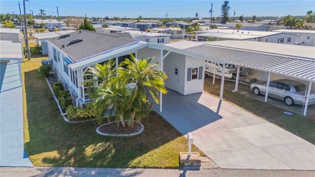 An elevated exterior view of a manufactured home with a carport, driveway, and palm trees — 527 FLEETWOOD STREET, NORTH PORT, FL