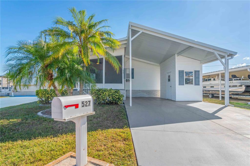 A white manufactured home features a carport, a screened porch, and a palm tree — 527 FLEETWOOD STREET, NORTH PORT, FL
