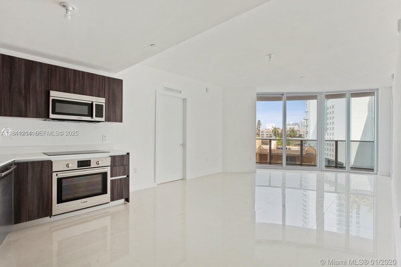 A modern kitchen with dark wood cabinets and stainless steel appliances opens to a living area — 488 NE 18th St # 501, Miami FL 33132, MIAMI, FL