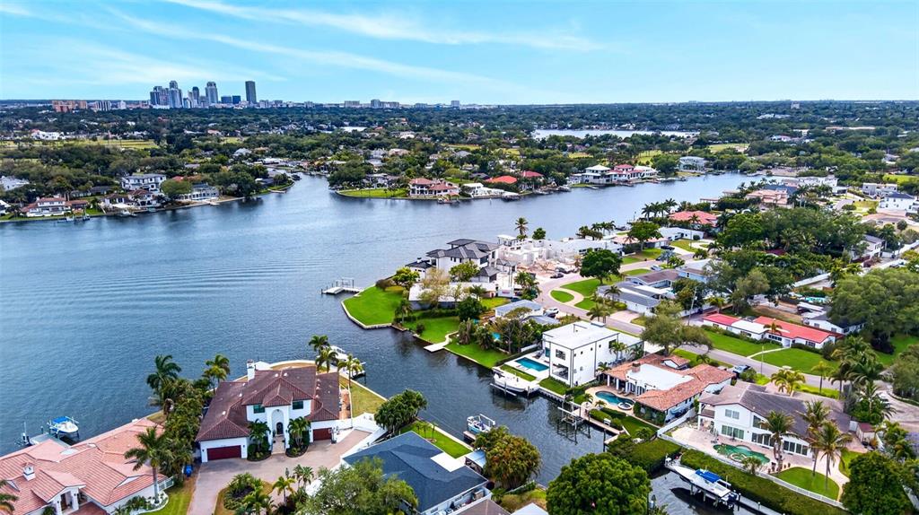 An aerial view shows waterfront luxury homes along a canal with a city skyline background — 874 PLACIDO WAY NE, ST PETERSBURG, FL