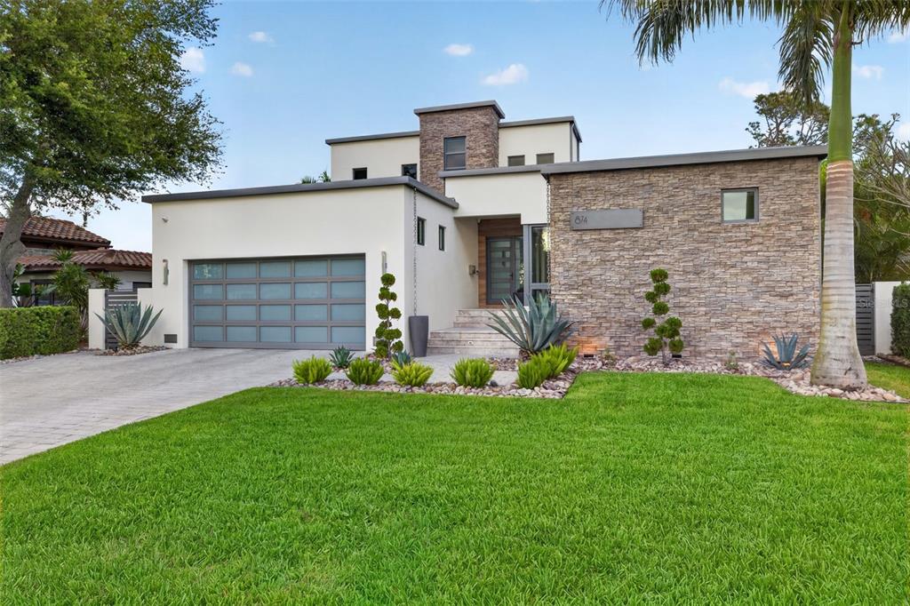 A modern two-story house features a stone facade, a gray garage door, and landscaped lawn — 874 PLACIDO WAY NE, ST PETERSBURG, FL