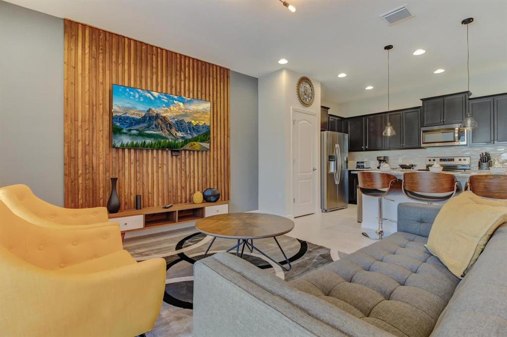 A living room with a wood-slat accent wall, yellow armchairs, and an open kitchen — 2436 DUBAI STREET, KISSIMMEE, FL