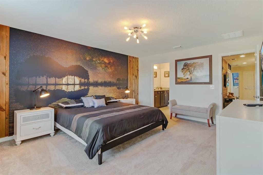 A bedroom features a large landscape mural behind the bed, wood accents, and neutral carpeting — 2436 DUBAI STREET, KISSIMMEE, FL