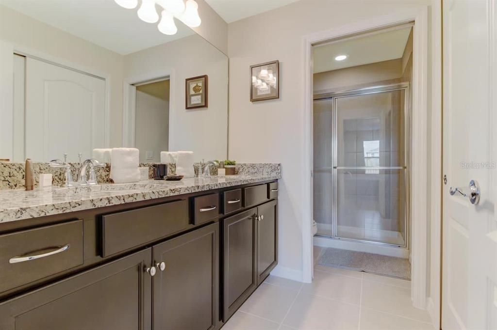 A bathroom features a dark wood vanity with a granite countertop and a glass shower — 2436 DUBAI STREET, KISSIMMEE, FL