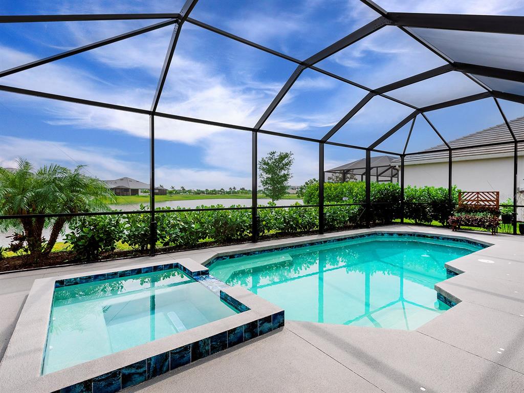 A screened-in pool and spa area with a view of a lake and landscaping — 10019 DEGAS TERRACE, BRADENTON, FL