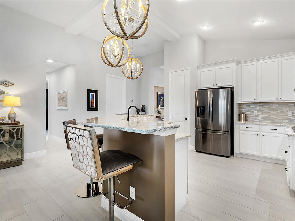 A kitchen features white cabinets, stainless steel appliances, a granite island, and pendant lighting — 10019 DEGAS TERRACE, BRADENTON, FL