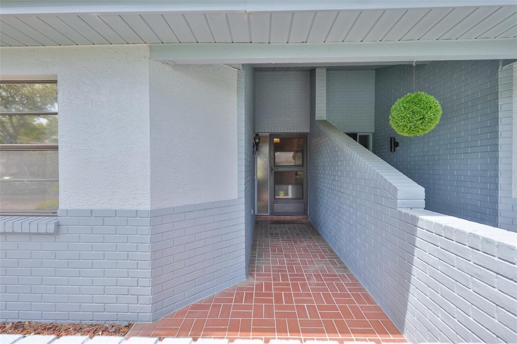 A covered entryway features a brick walkway leading to a glass-paned front door — 1618 LELAND DRIVE, SUN CITY CENTER, FL