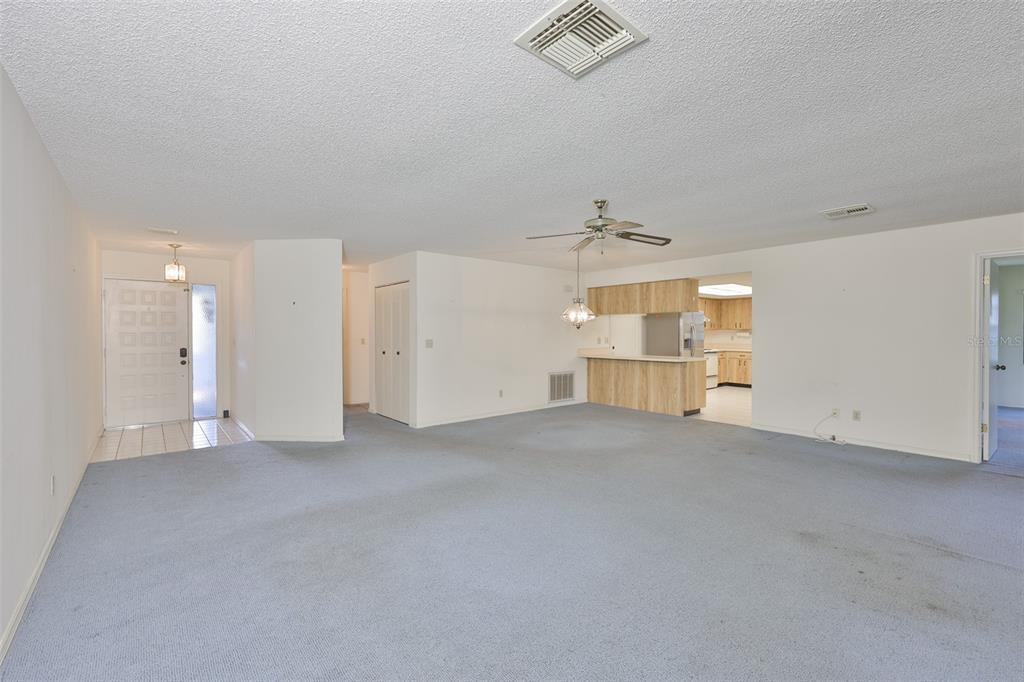 A spacious living room with blue carpet, a ceiling fan, and an open kitchen area — 1618 LELAND DRIVE, SUN CITY CENTER, FL