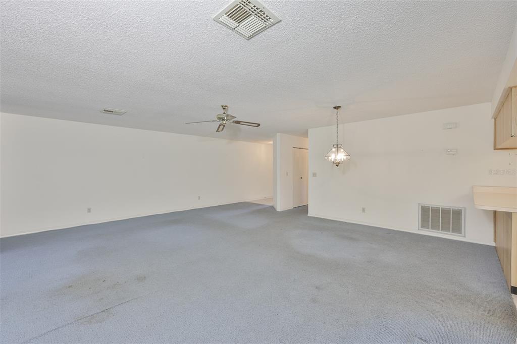 A spacious room with light blue carpeting, a ceiling fan, and a dining area chandelier — 1618 LELAND DRIVE, SUN CITY CENTER, FL