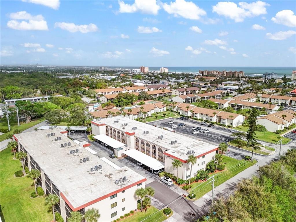 An aerial view shows multi-story apartment buildings with flat roofs and parking lots near the coast — 5800 N BANANA RIVER BOULEVARD UNIT 134, CAPE CANAVERAL, FL