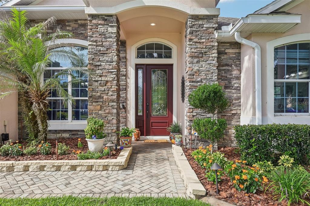 A stone-accented house exterior features a red front door, arched windows, and a brick walkway — 115 W BLUE WATER EDGE DRIVE, EUSTIS, FL