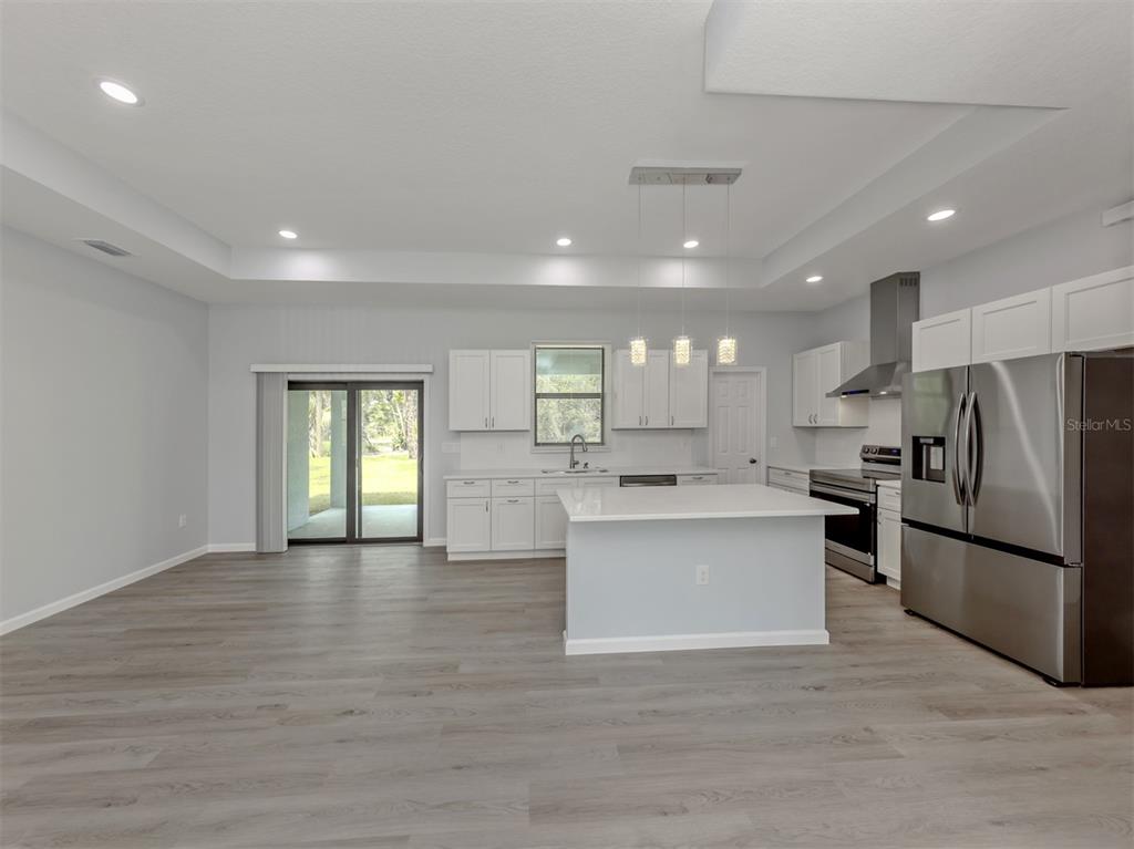 A modern kitchen features white cabinetry, stainless steel appliances, a central island, and wood-look flooring — 3763 RAGEN STREET, NORTH PORT, FL