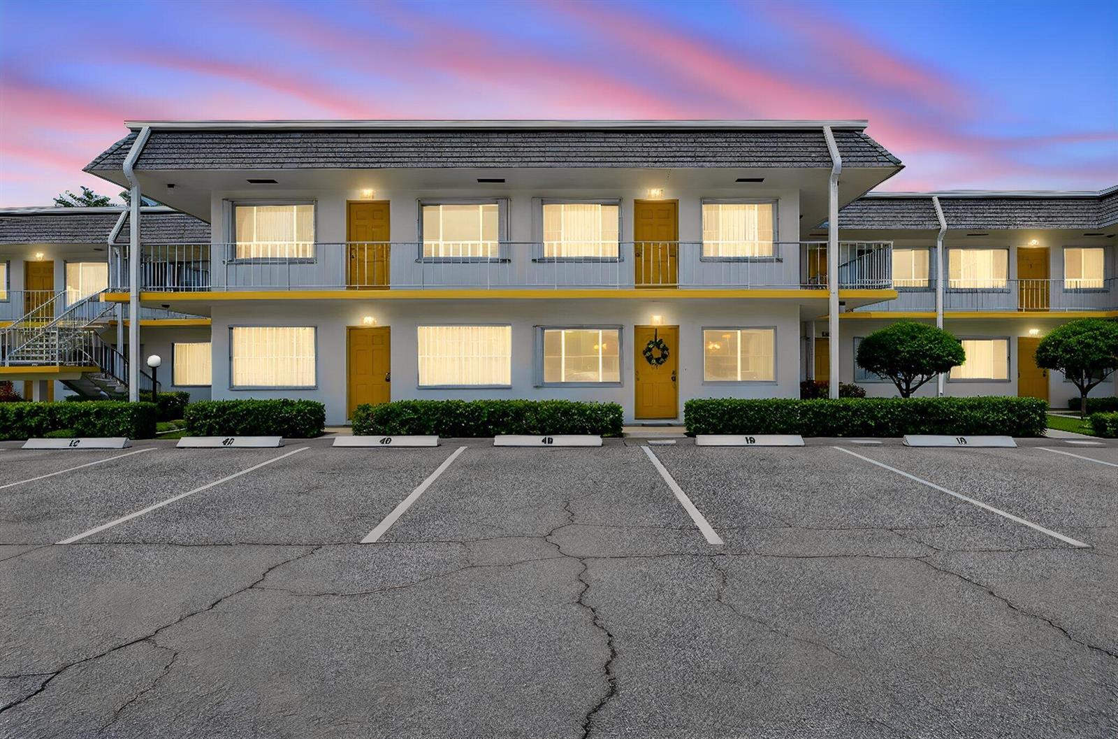 A two-story motel building with yellow doors and a parking lot in the foreground — 3240 Lake Osborne Drive Apt 104, FL 33461, FL