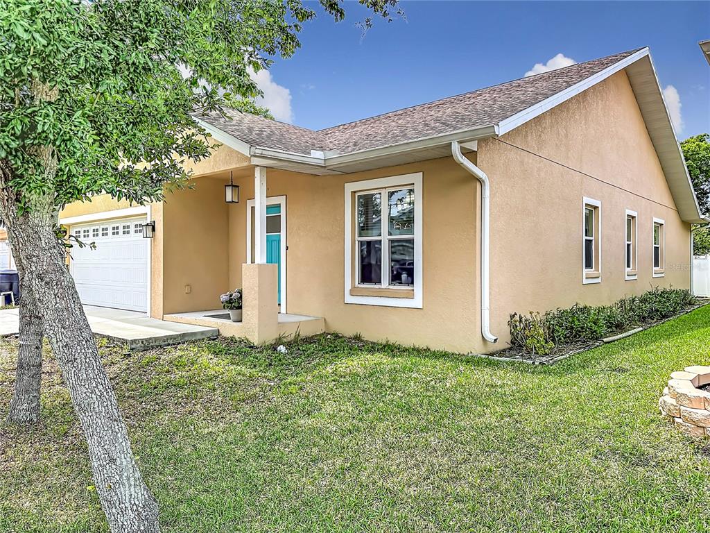 A tan, single-story house with a white garage door, a covered entryway, and a grassy lawn — 1590 BURNS DRIVE, CLEARWATER, FL