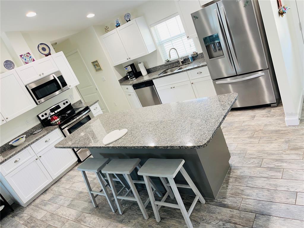 A kitchen features white cabinets, granite countertops, stainless steel appliances, and a gray center island — 7076 NICHOLS STREET, ENGLEWOOD, FL