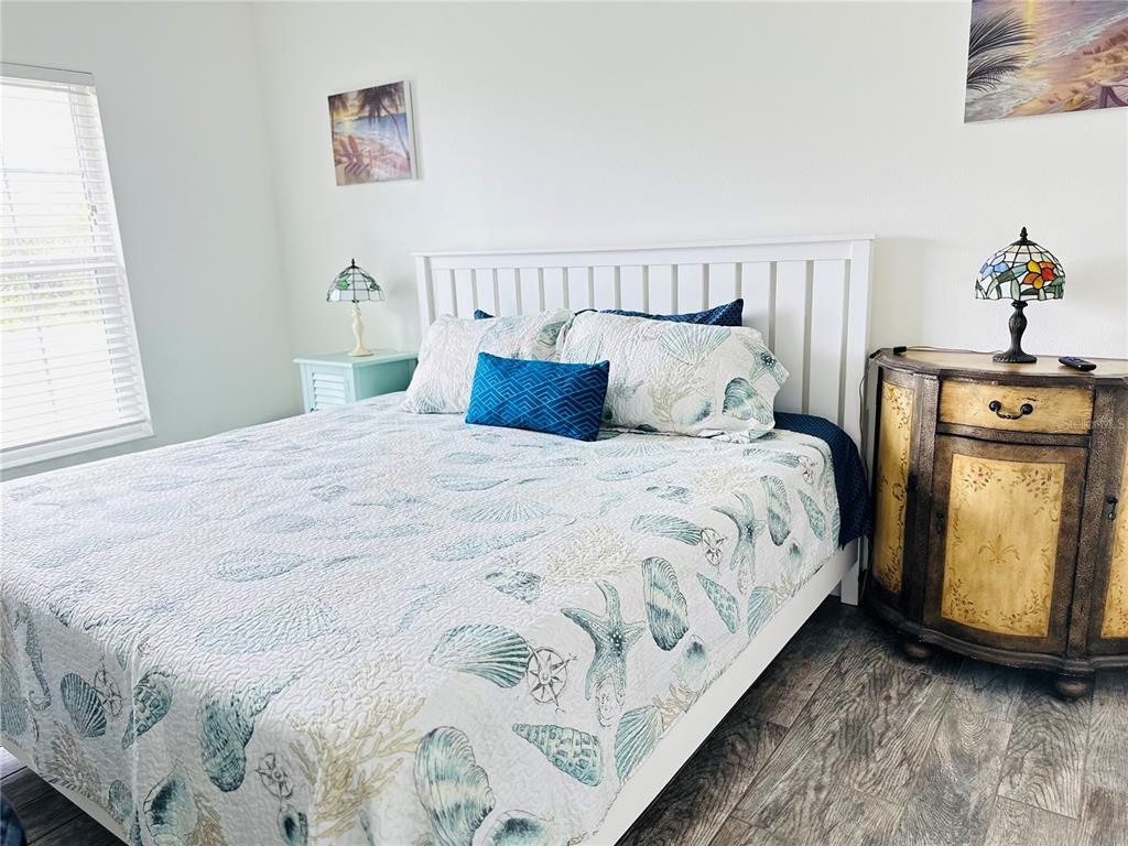 A bedroom features a white bed with seashell-patterned bedding, two stained-glass lamps, and wood flooring — 7076 NICHOLS STREET, ENGLEWOOD, FL