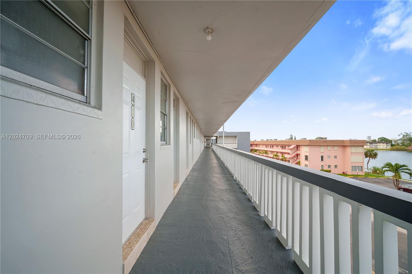 An outdoor apartment walkway features a white door, a gray floor, and a white railing — 18601 NE 14th Ave # 409, Miami FL 33179, MIAMI, FL