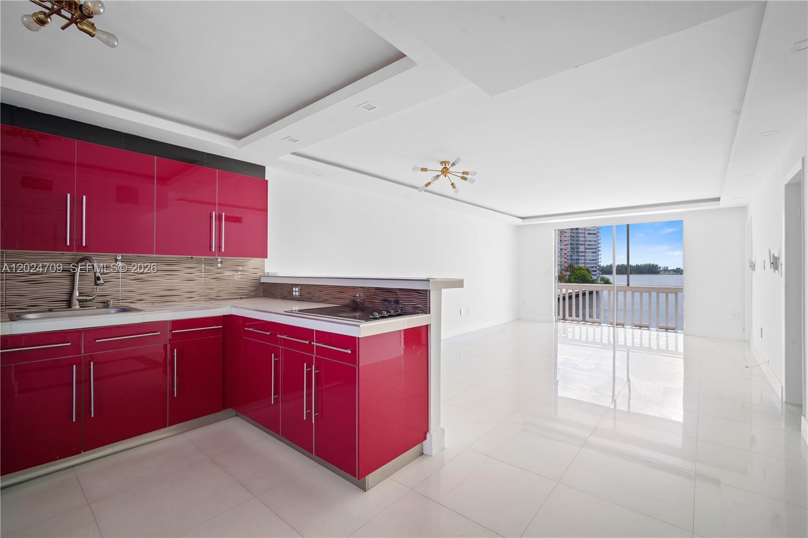 A kitchen with glossy magenta cabinets and white tile floors opens to a waterfront balcony — 18601 NE 14th Ave # 409, Miami FL 33179, MIAMI, FL
