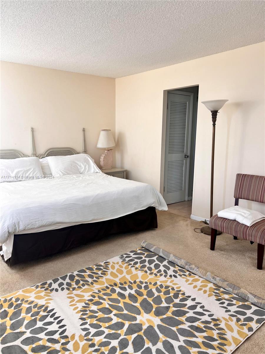 A bedroom features a bed with a white comforter, a patterned rug, and a floor lamp — 1410 S Ocean Dr # 804, Hollywood FL 33019, HOLLYWOOD, FL