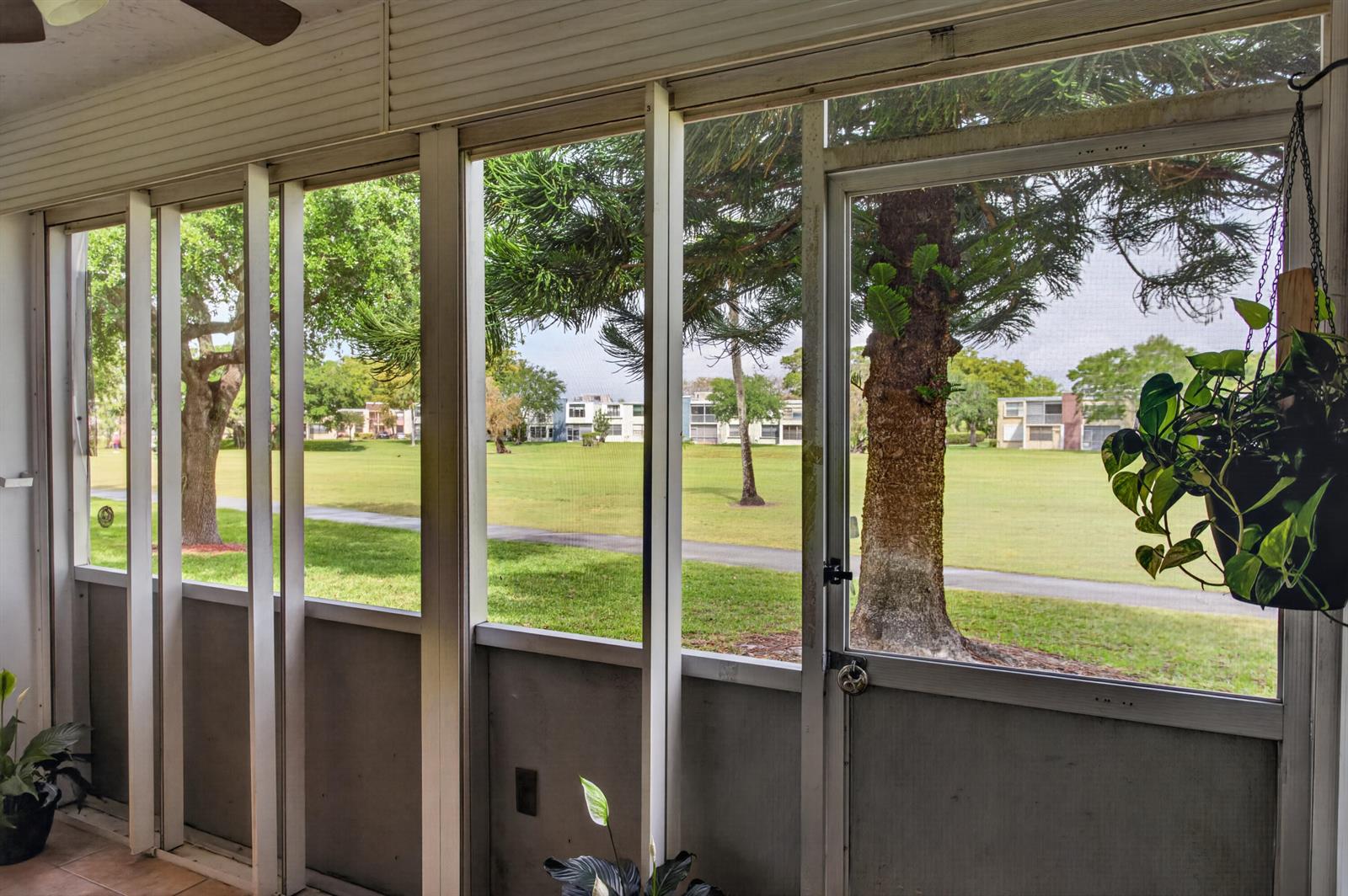 A screened-in porch overlooks a grassy lawn with trees and distant apartment buildings — 7321 NW 18th Street # 107, Margate FL 33063, MARGATE, FL