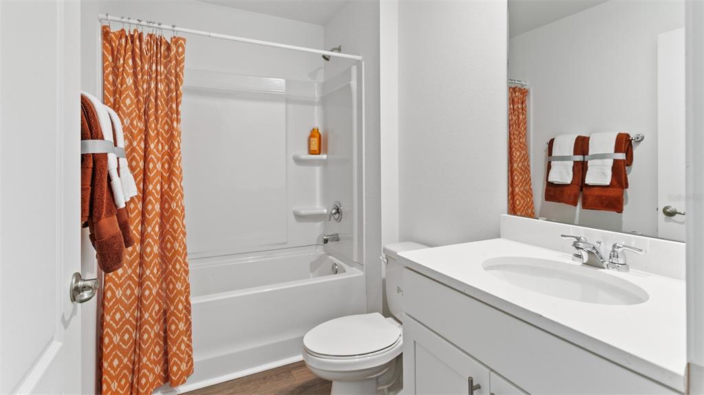 A bathroom features a white vanity, a toilet, and a shower-tub combo with orange curtains — 32 HARDWOOD TRAIL, PALM COAST, FL