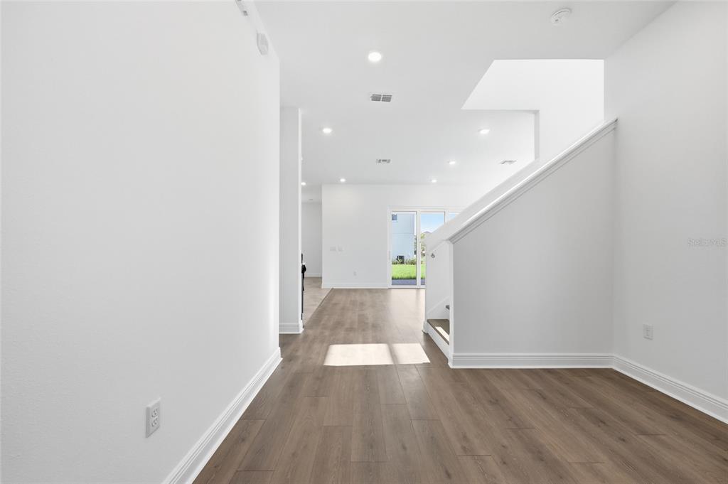 A bright entryway features wood-look flooring, white walls, and a staircase with a white railing — 10085 BALLAST DRIVE, ORLANDO, FL