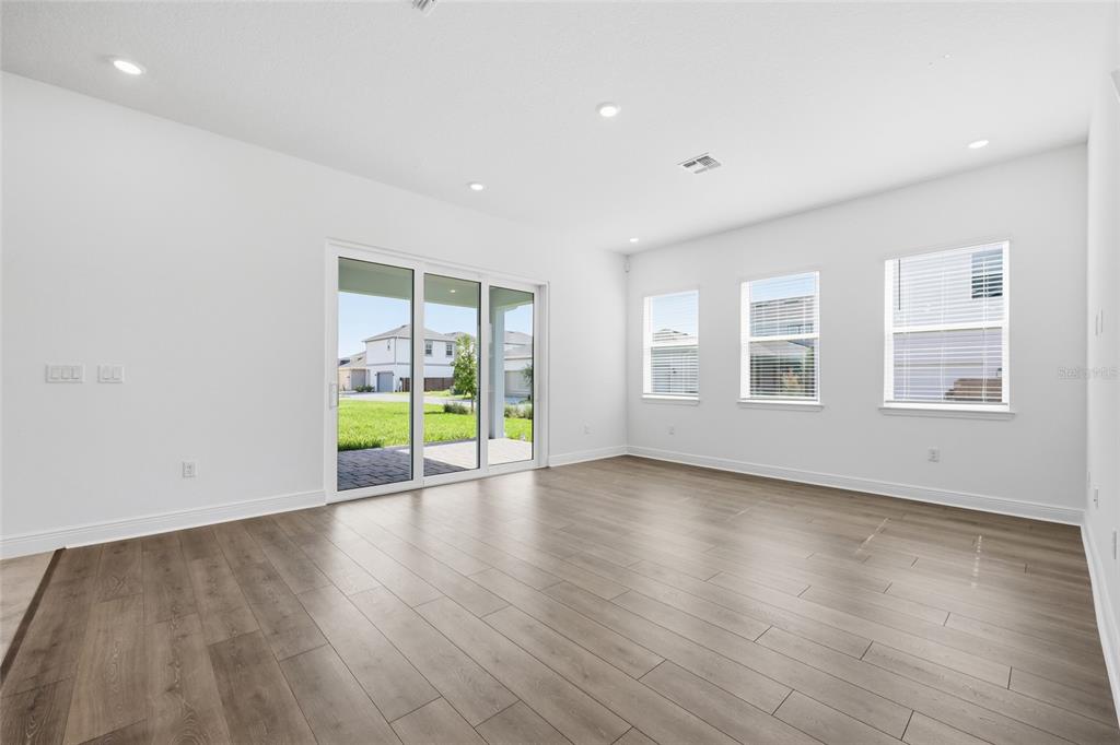 A bright, empty living room features light wood-look flooring, white walls, and large sliding glass doors — 10085 BALLAST DRIVE, ORLANDO, FL