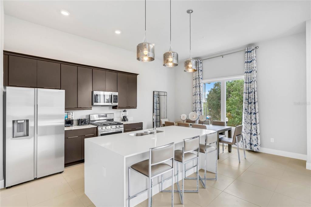 A modern kitchen features dark brown cabinets, a white island with bar seating, and pendant lights — 7740 SANDY RIDGE DRIVE 241 BLDG 44, REUNION, FL